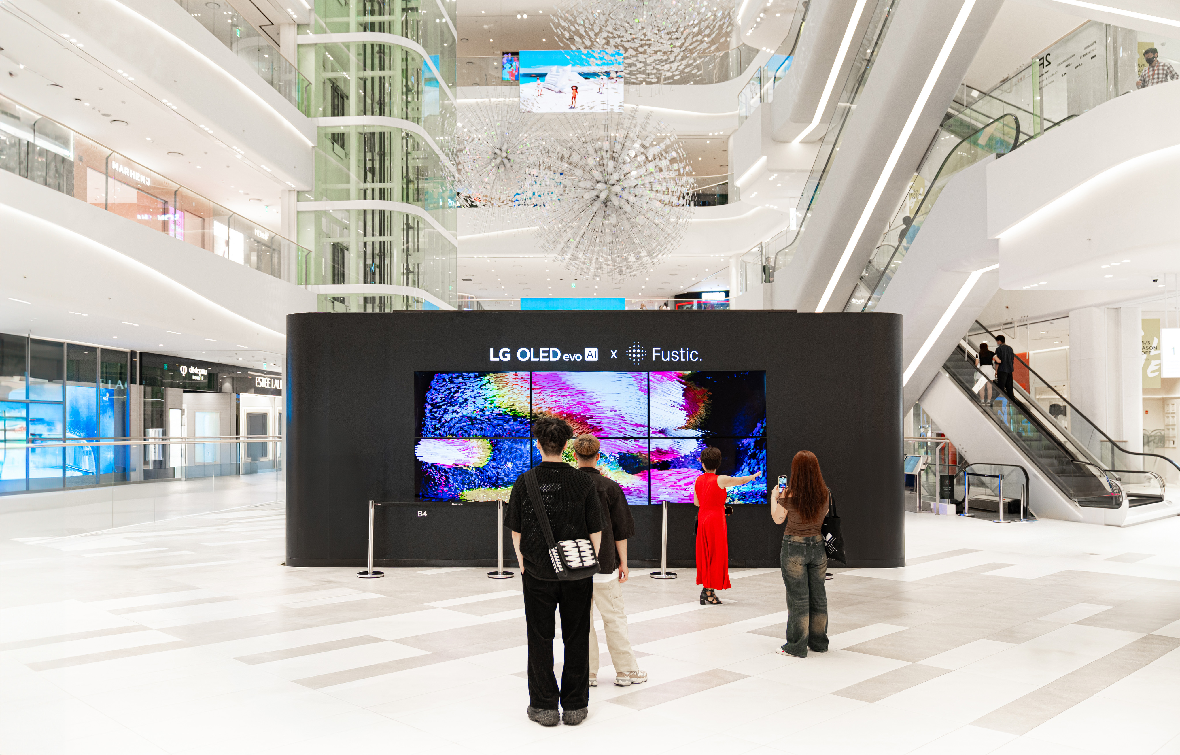 Visitors observe the 'Futurescape' installation in the Lotte Mall West Lake. A large black display features a multi-screen interactive experience showing vibrant, abstract generative art.