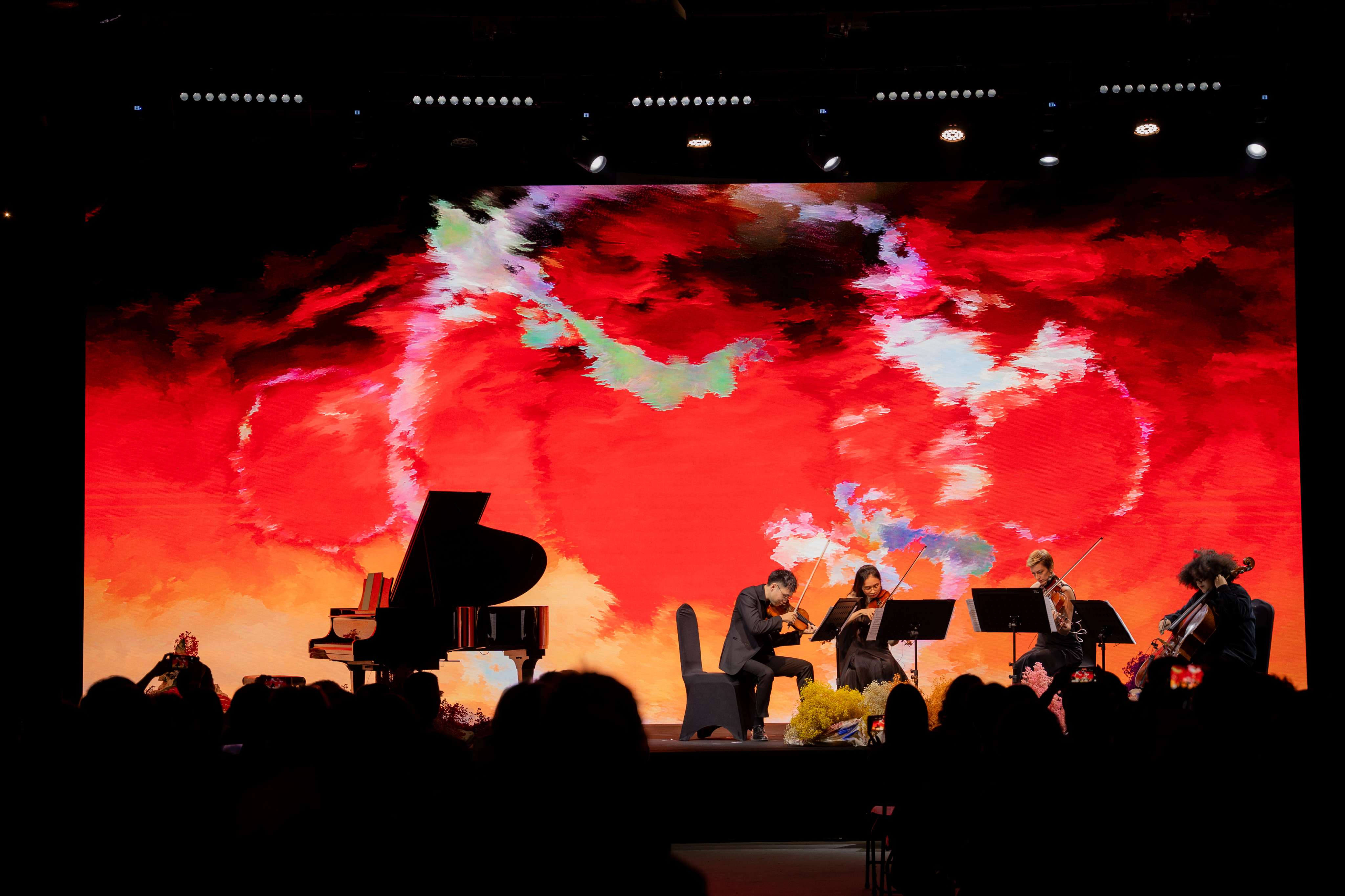 A string quartet plays passionately, framed by an intense, fiery red and orange abstract digital canvas on the main screen.