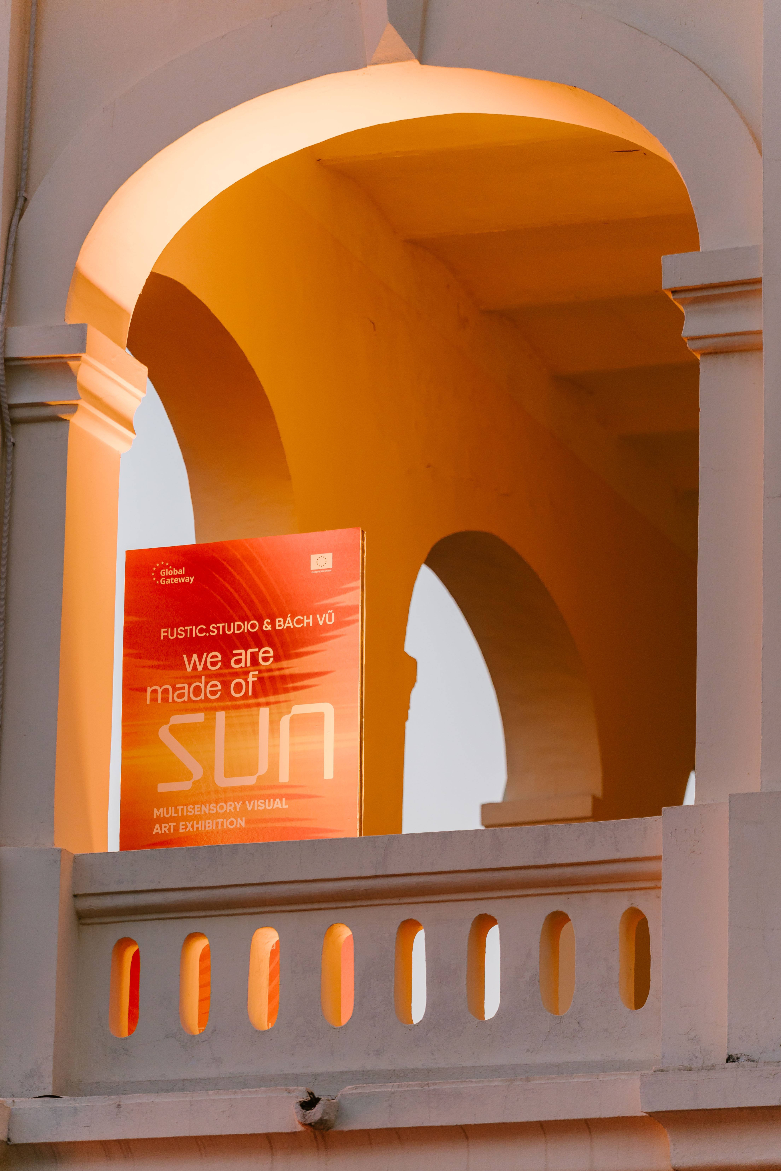 An promotional poster of 'We Are Made of Sun' Exhibition by resting on a white, arched balcony.